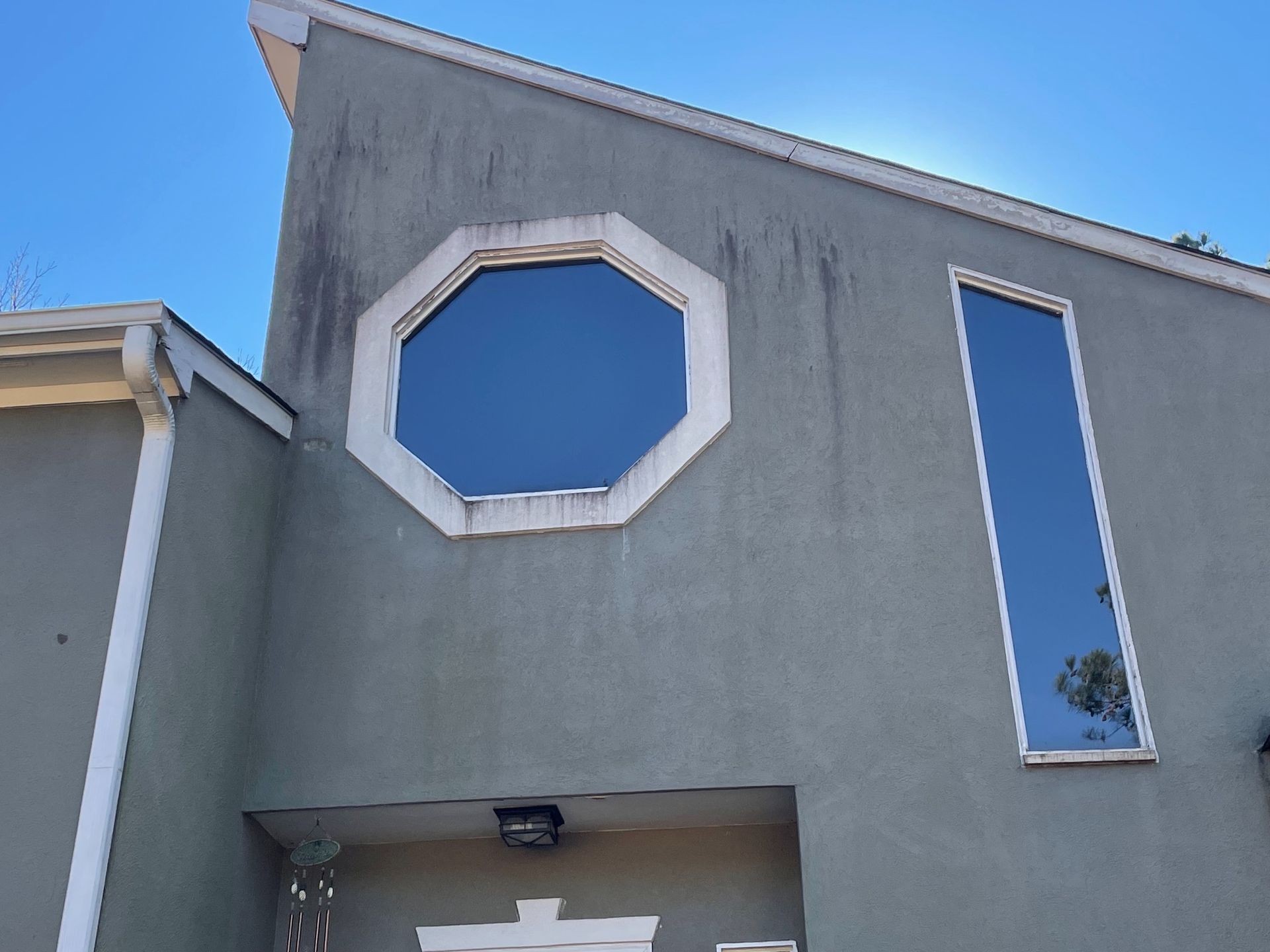 Gray stucco house facade with octagonal and narrow vertical windows against a blue sky