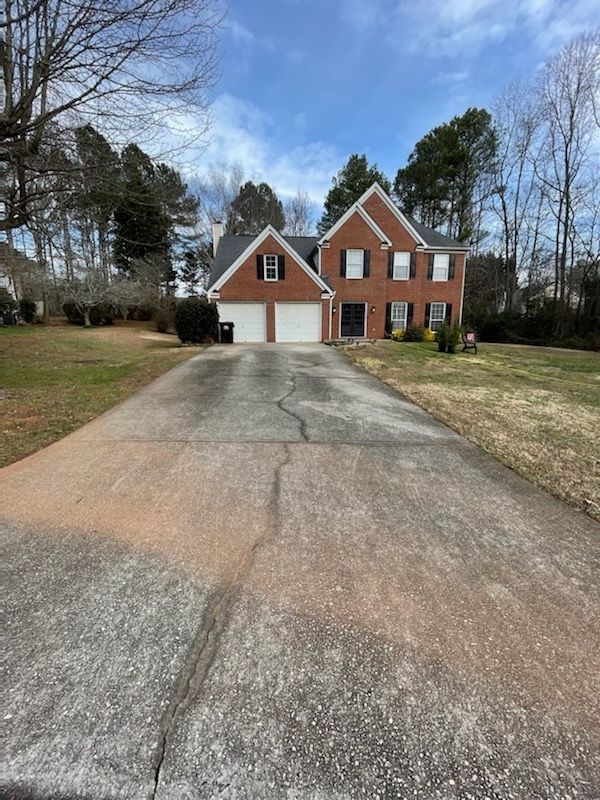 Brick suburban house with two-car garage and long driveway under a partly cloudy sky