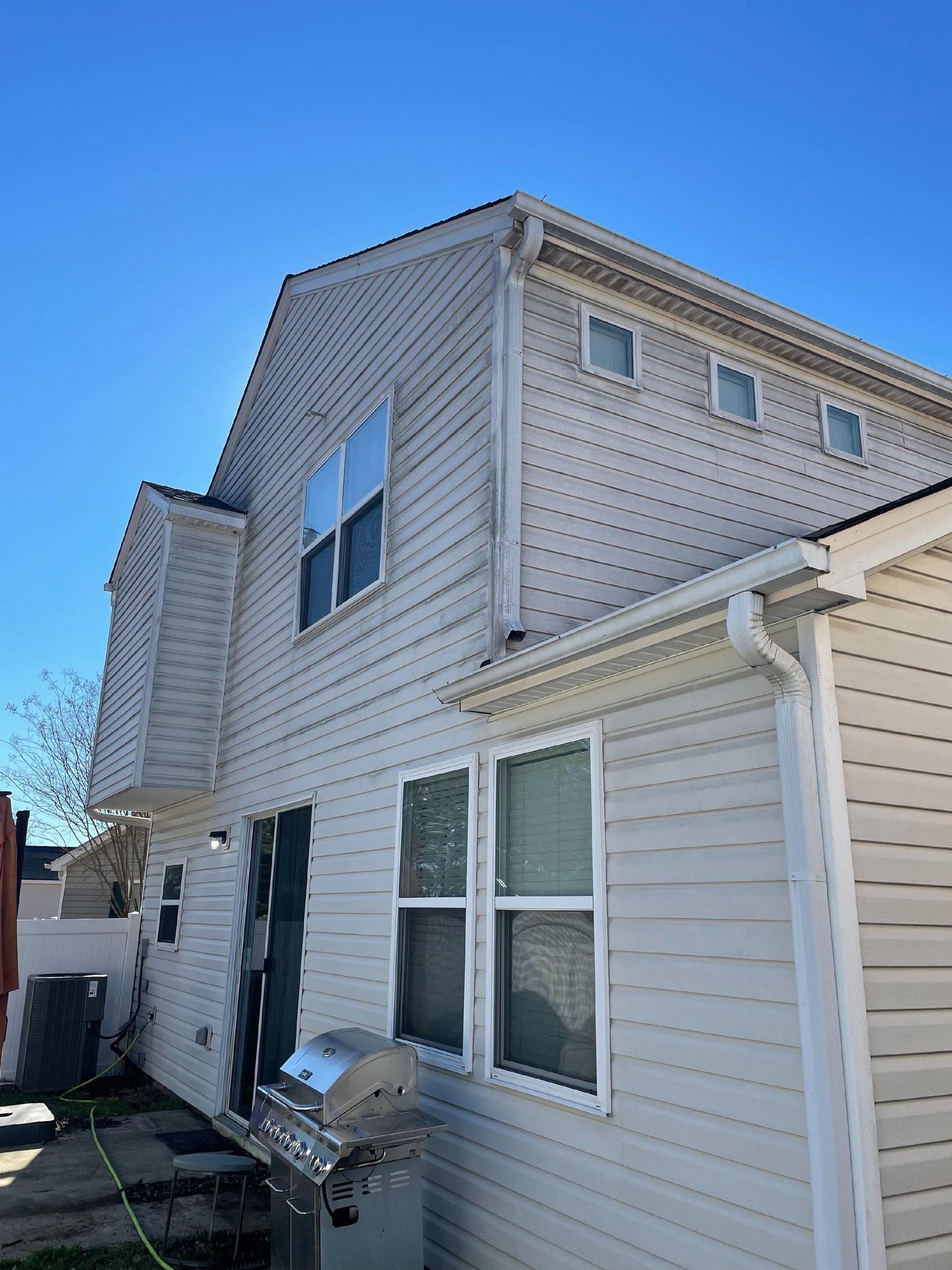 Side of a white house with vinyl siding, windows, and a small deck against a blue sky.