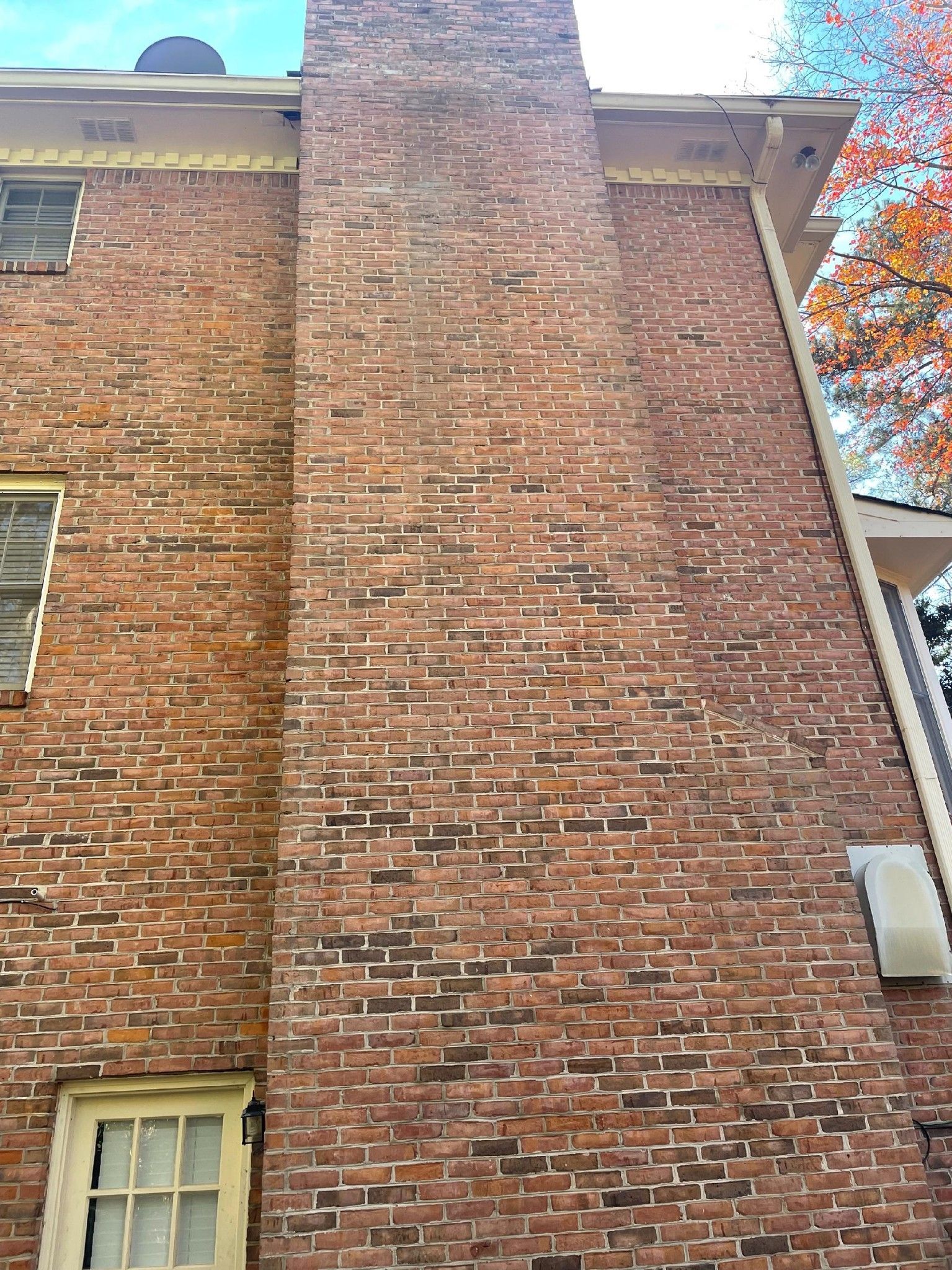 Tall brick building wall with a central chimney and a small window near the bottom, viewed from below