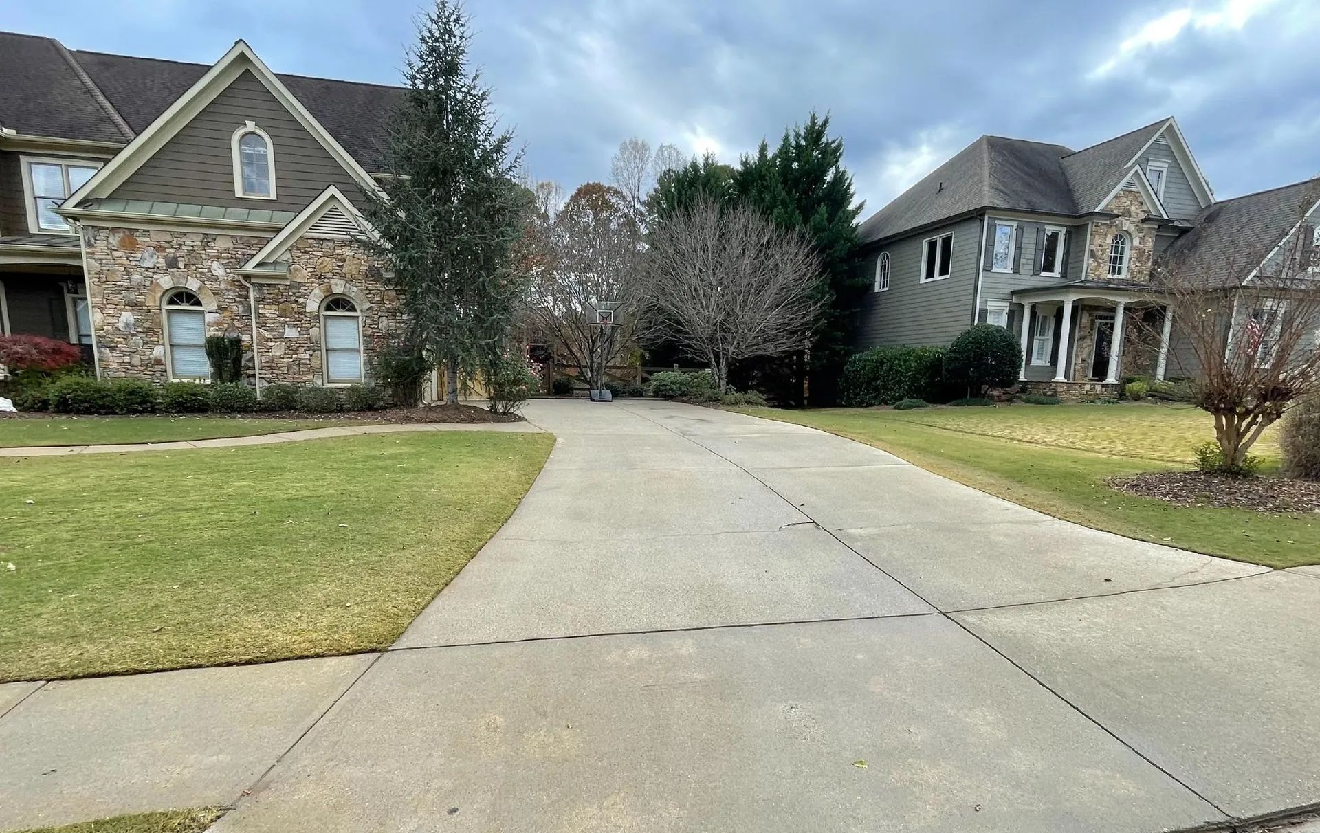 Suburban driveway between two stone houses with lawns and trees