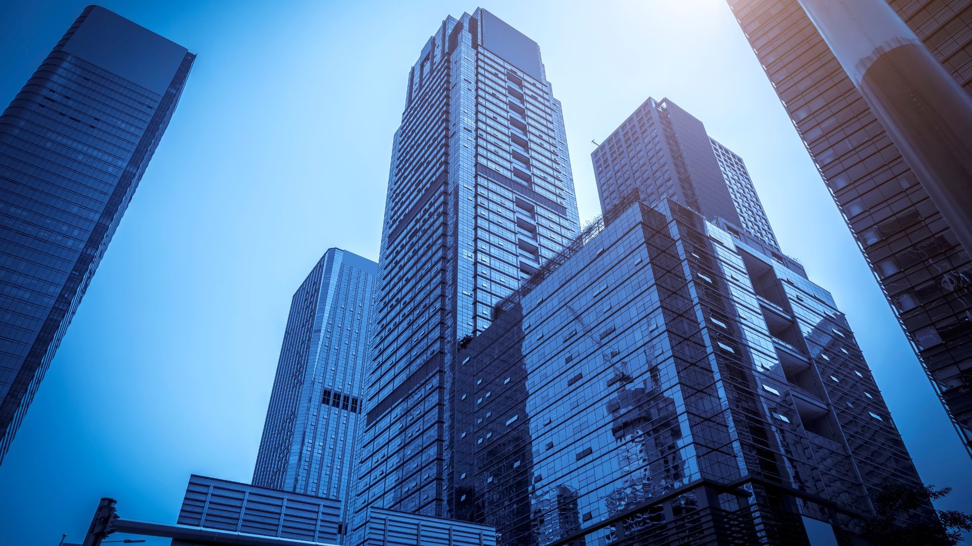 Tall glass skyscrapers against a bright blue sky, viewed from below