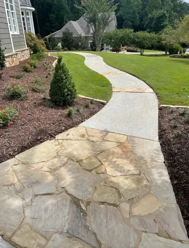Curved concrete walkway through a landscaped yard with stone pavers and green lawn around a house