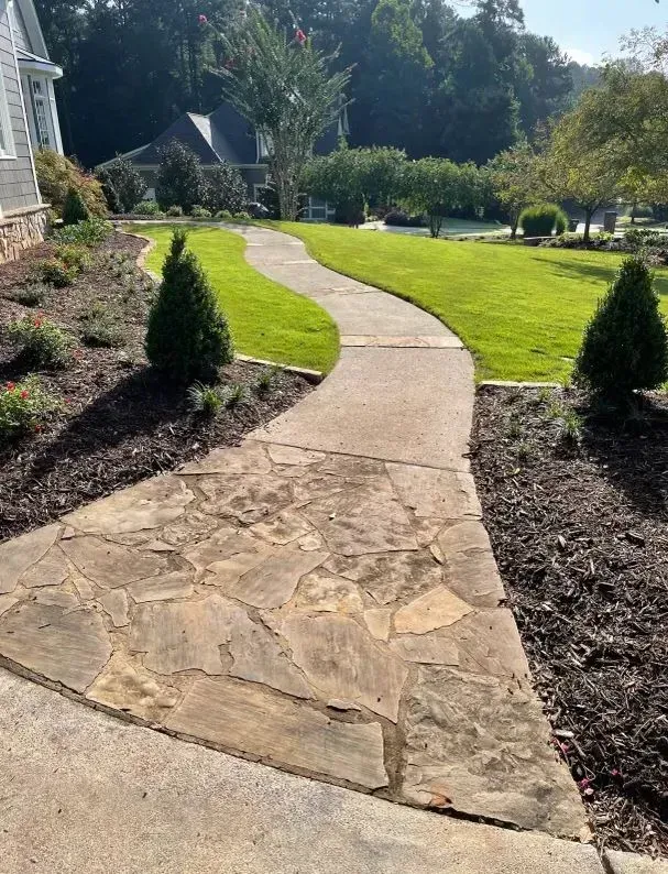 Stone garden path curving through a green lawn with shrubs and trees in bright sunlight