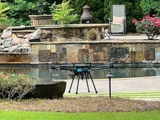 Small drone on a tripod by a backyard pond with stone landscaping and flowers