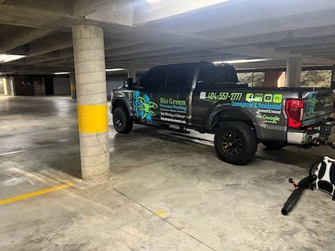 Black pickup truck with company graphics parked in a concrete parking garage, with a dog on a leash nearby.