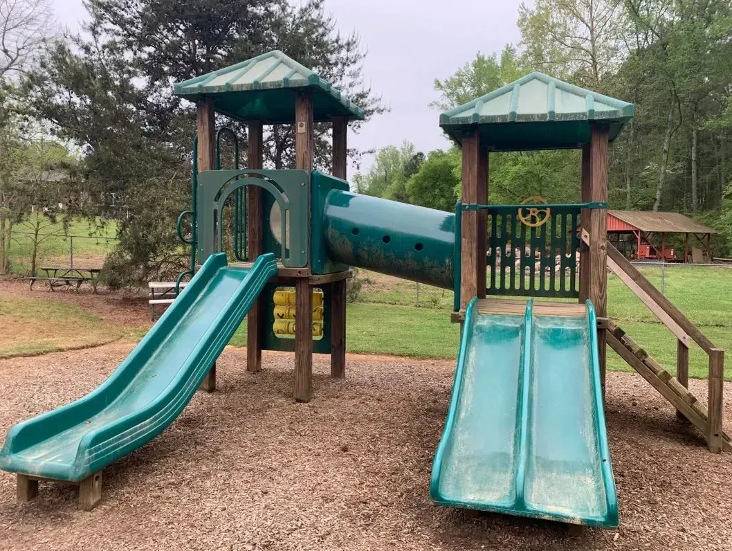 Children’s playground with two teal slides and green-roofed towers on a woodchip surface.
