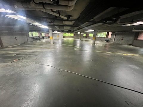 Empty indoor parking garage with wet concrete floor and overhead pipes