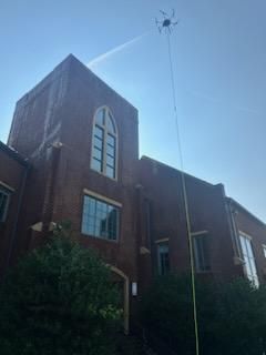 Red brick church tower with arched window, seen from below against a bright blue sky.