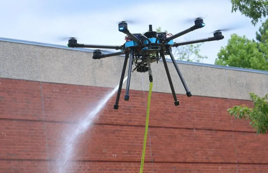 Drone spraying water onto a brick wall; outdoors, daytime.