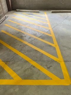 Yellow diagonal hatch markings painted on a concrete parking bay or no-parking zone.