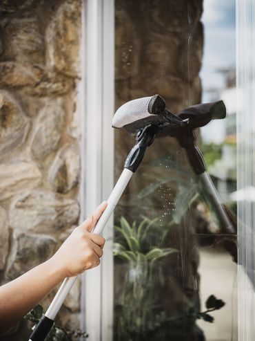 Hand using a squeegee to clean a glass door beside a stone wall