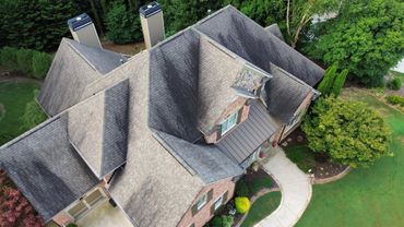 Aerial view of a brick house with a gray roof and landscaped yard surrounded by trees.