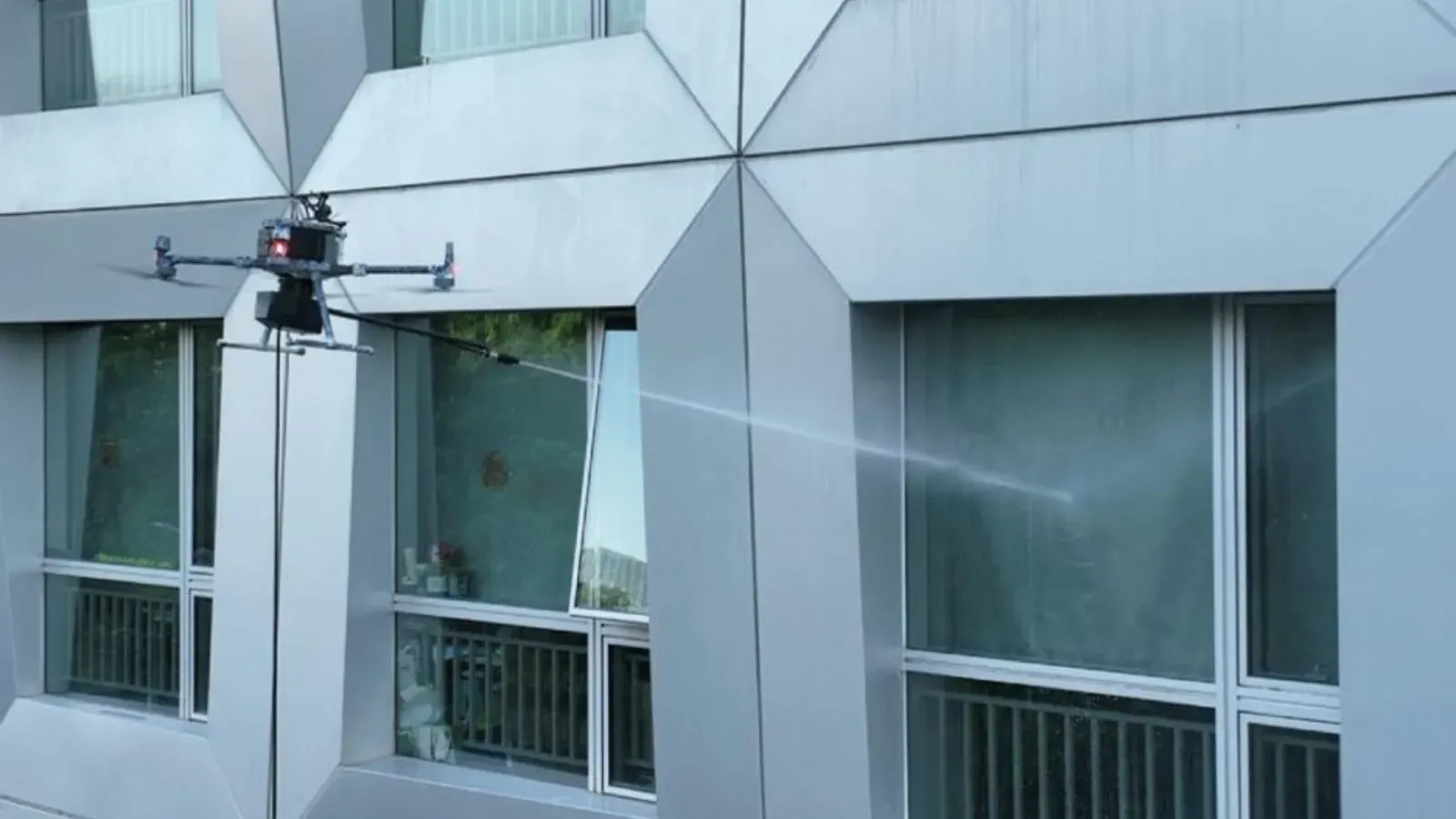 Drone spraying a mist near a building’s windows and facade