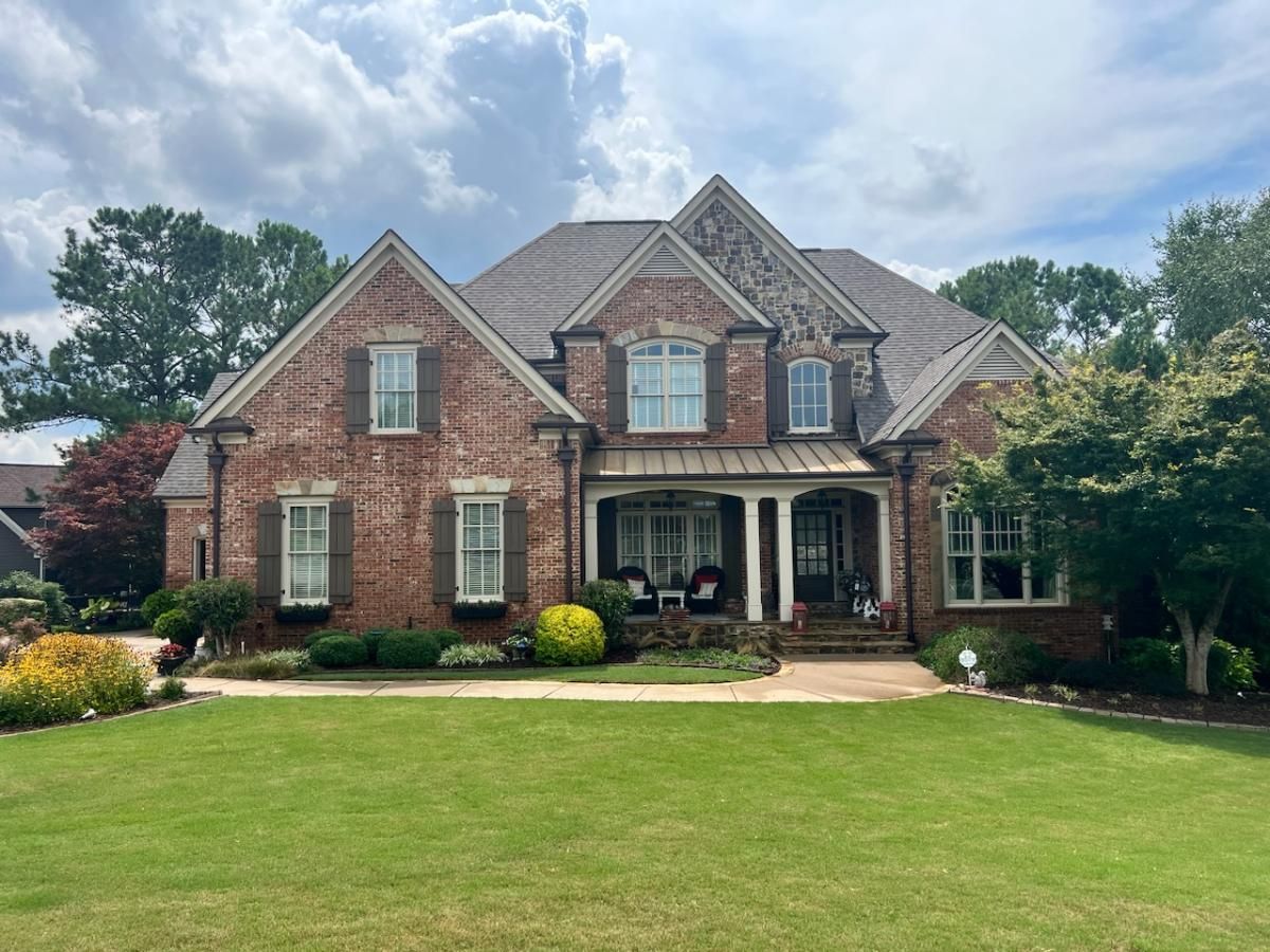 Brick two-story suburban house with manicured lawn, front porch, and gabled roof under a partly cloudy sky