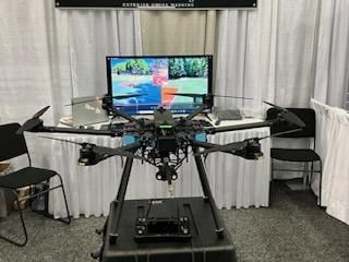 Drone rig in a room, mounted in front of a large monitor displaying a landscape scene.