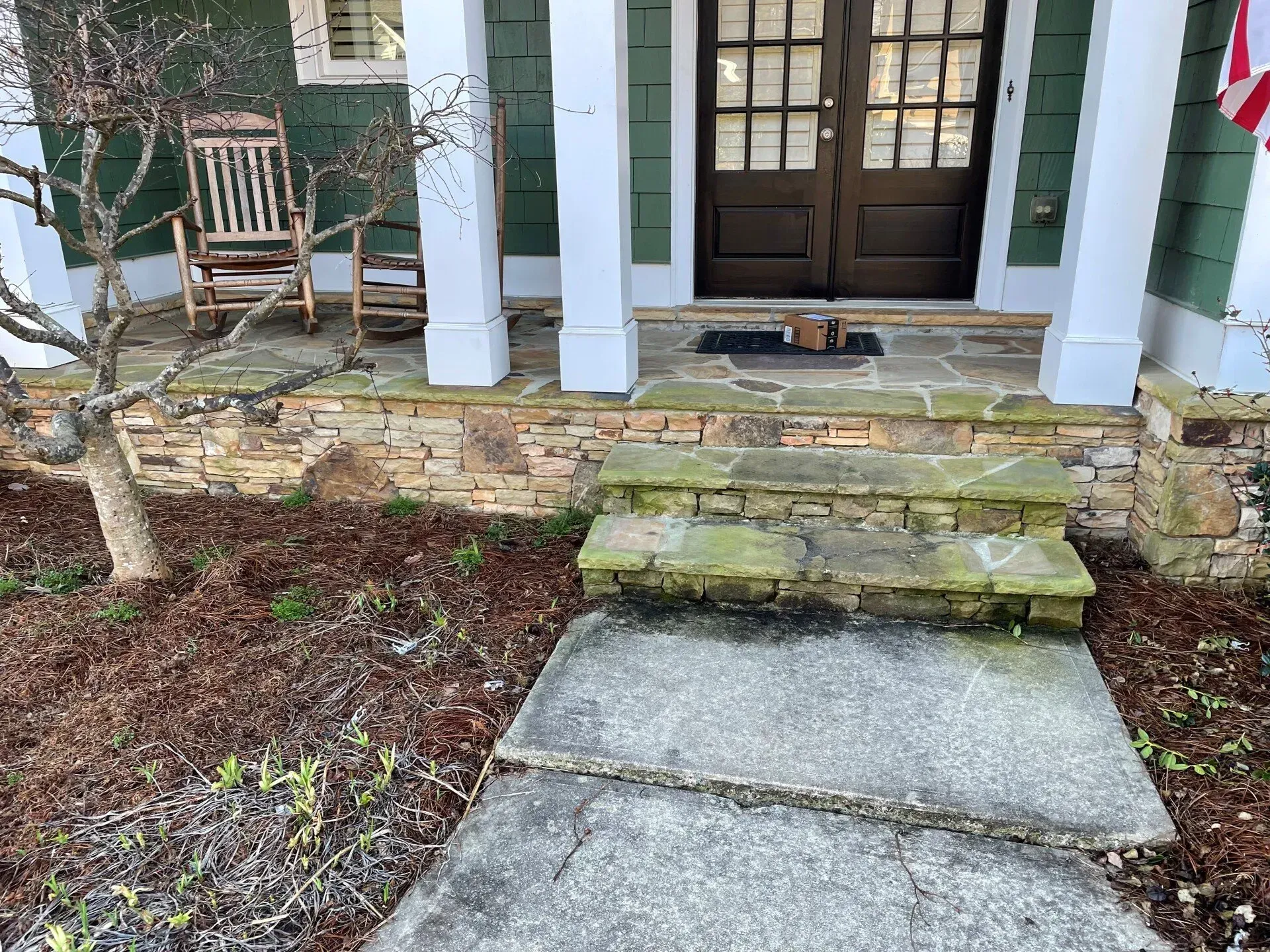 Front porch with stone steps and walkway leading to a dark double door, flanked by white columns and green shutters