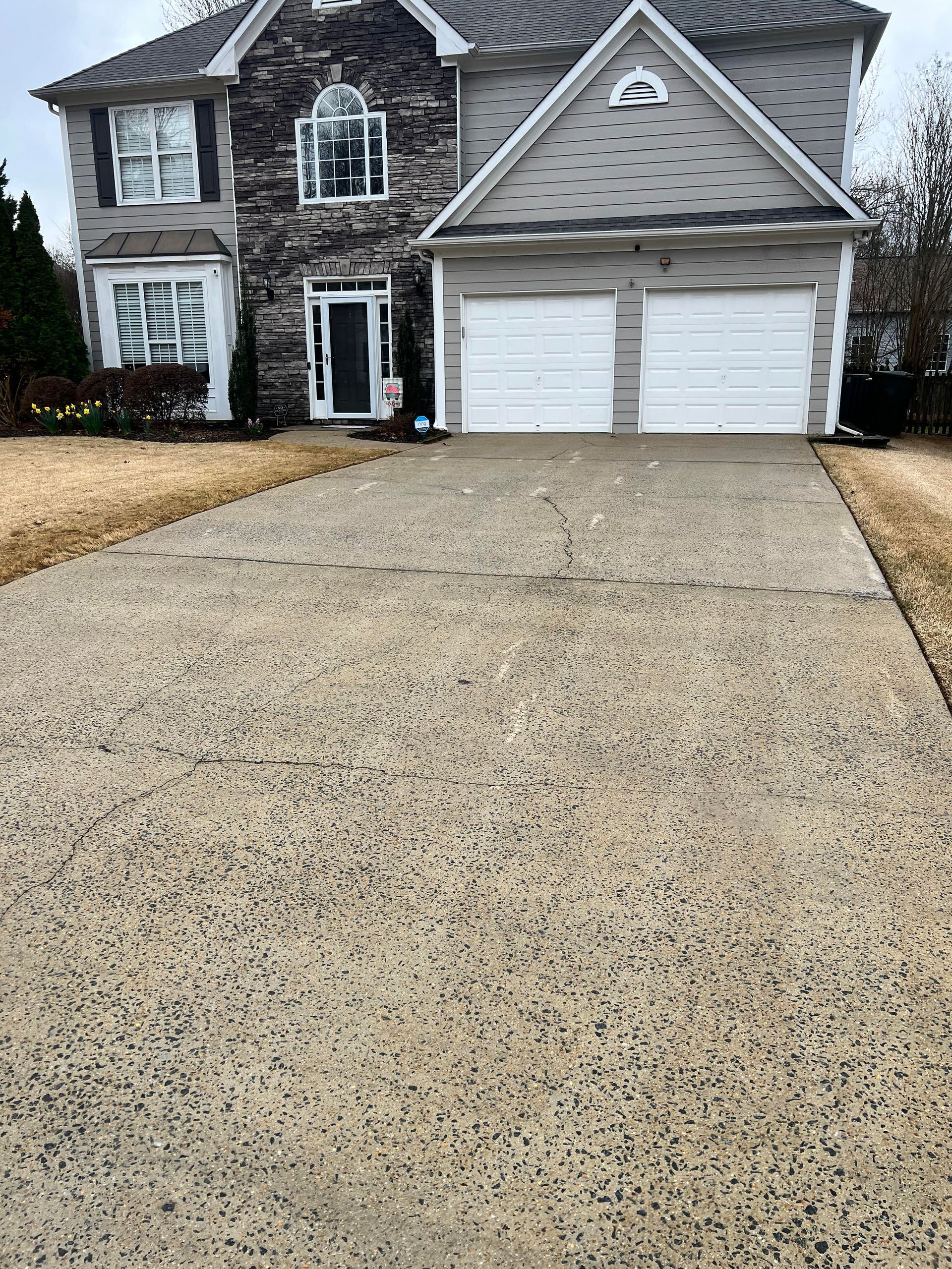 Suburban two-story brick house with a wide concrete driveway and double white garage doors