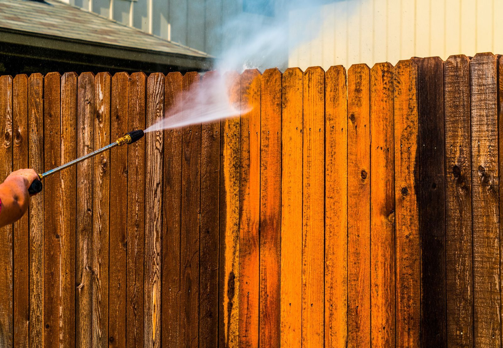 Person pressure-washing a wooden fence, with white spray cleaning the brown boards