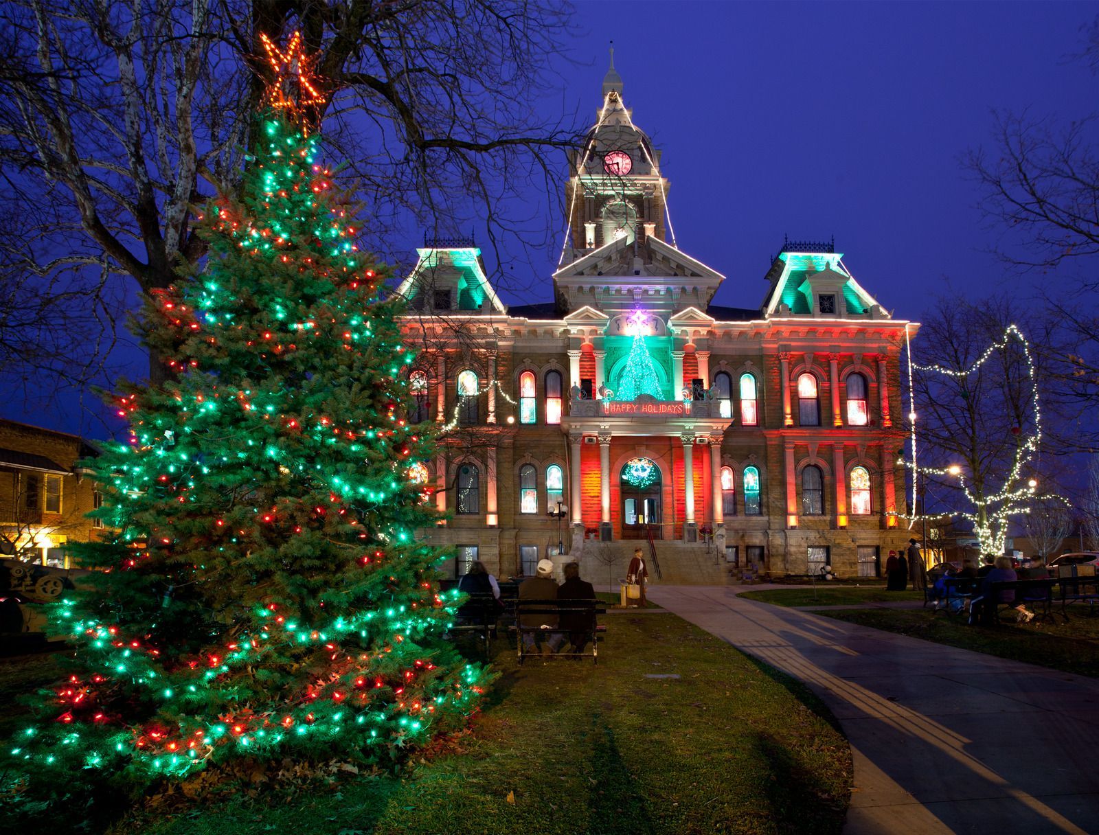 Holiday-lit historic building with a decorated Christmas tree at dusk