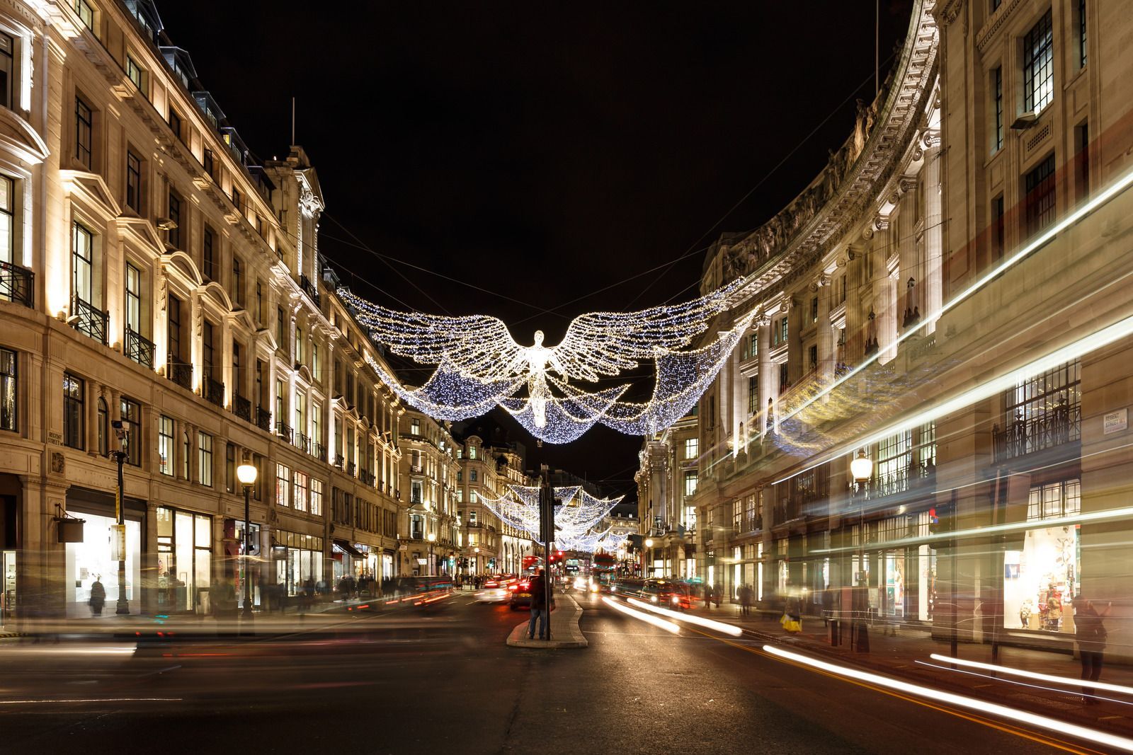 Night street scene with illuminated buildings and festive lights over a busy boulevard at dusk