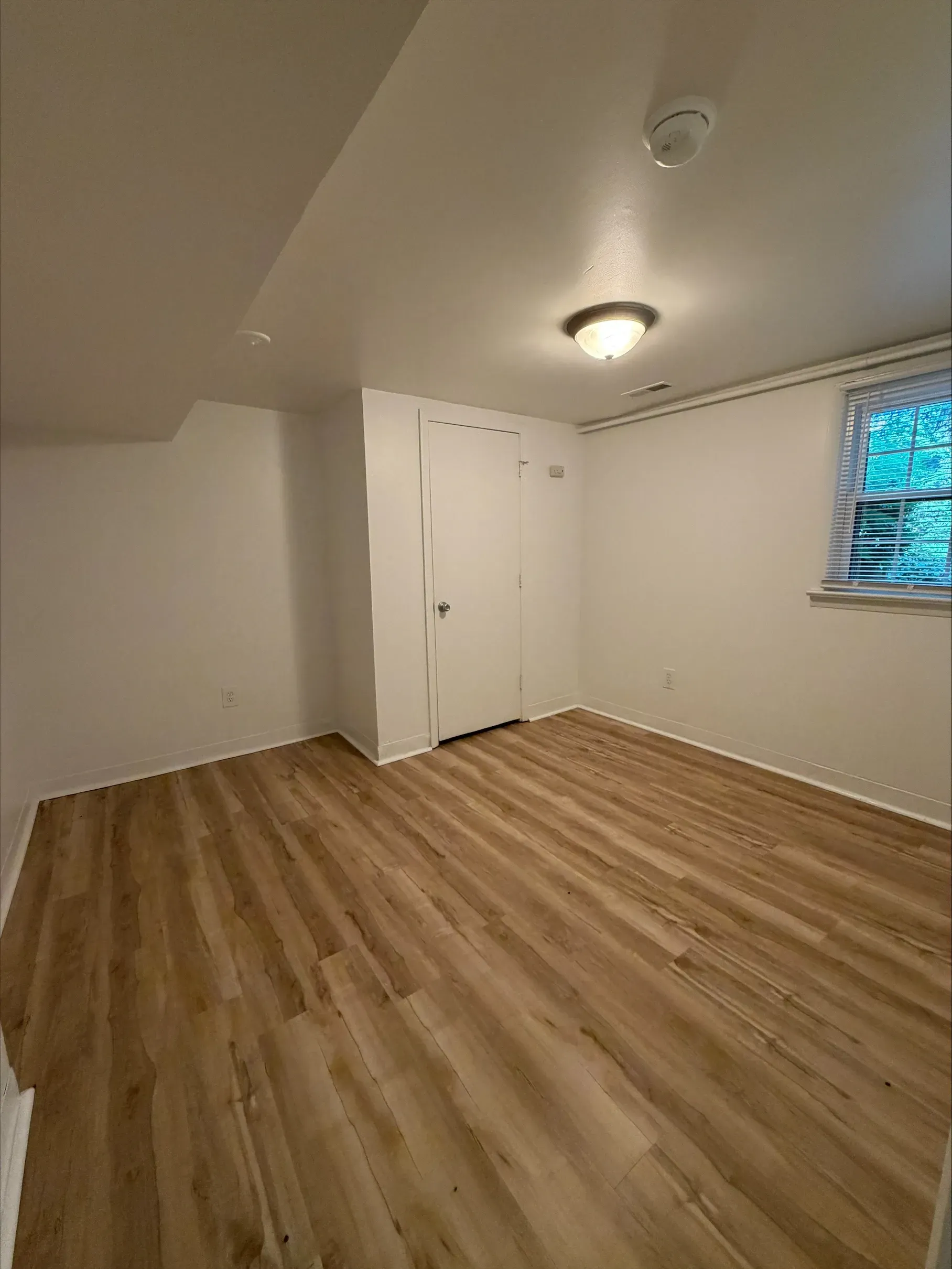 Empty unfurnished room with wood floor, white walls, closet, and small window.