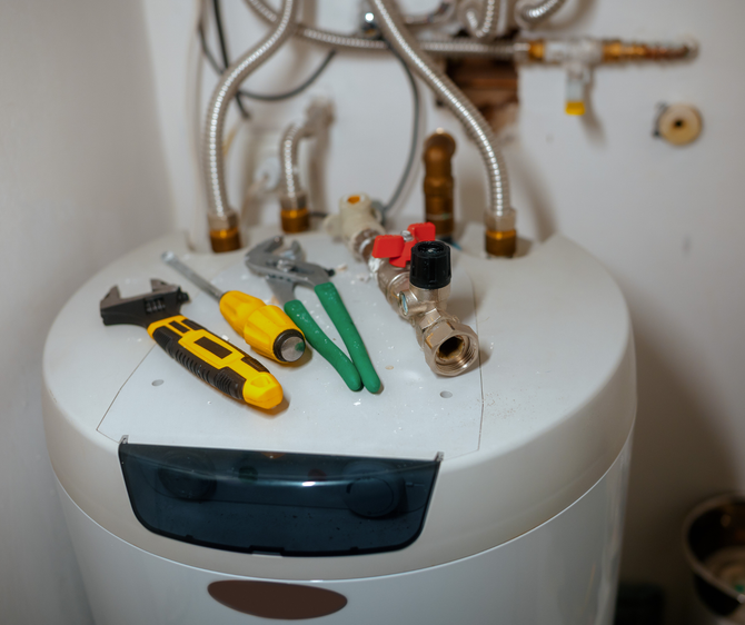 Tools rest on a water heater, suggesting repair or maintenance.