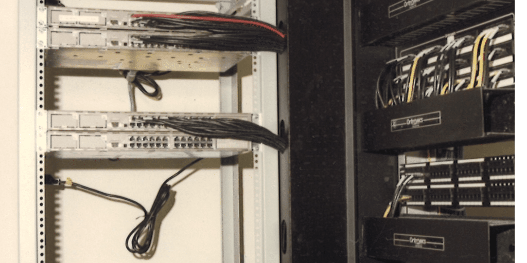 Server rack filled with network switches and patch panels, with tangled cables.