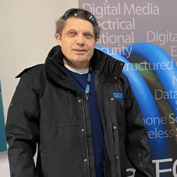 Man wearing a black jacket, standing in front of a banner with text.