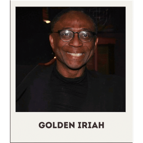 Golden Iriah, smiling Black man with glasses in front of a dark background, wearing a black jacket and shirt.