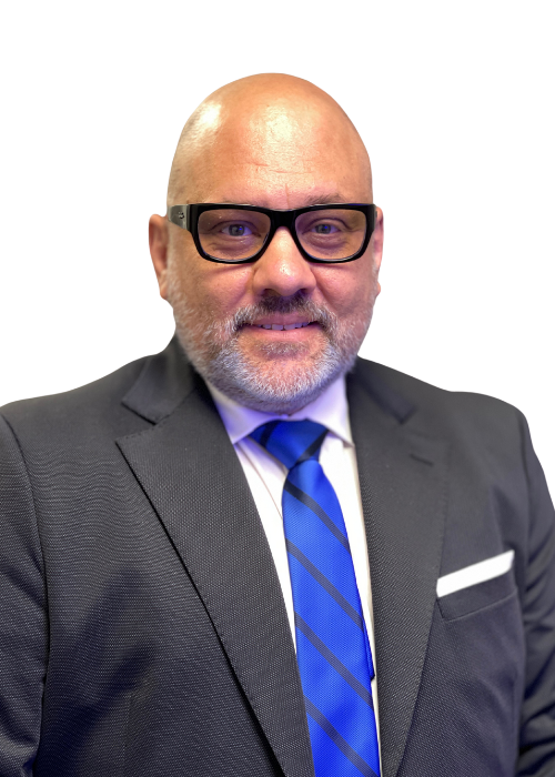 Man in suit and glasses smiles, with a blue tie.