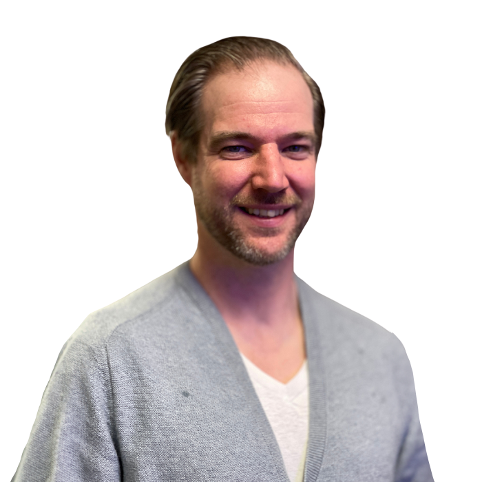 Man with fair skin, smiling, in light blue sweater and white shirt.