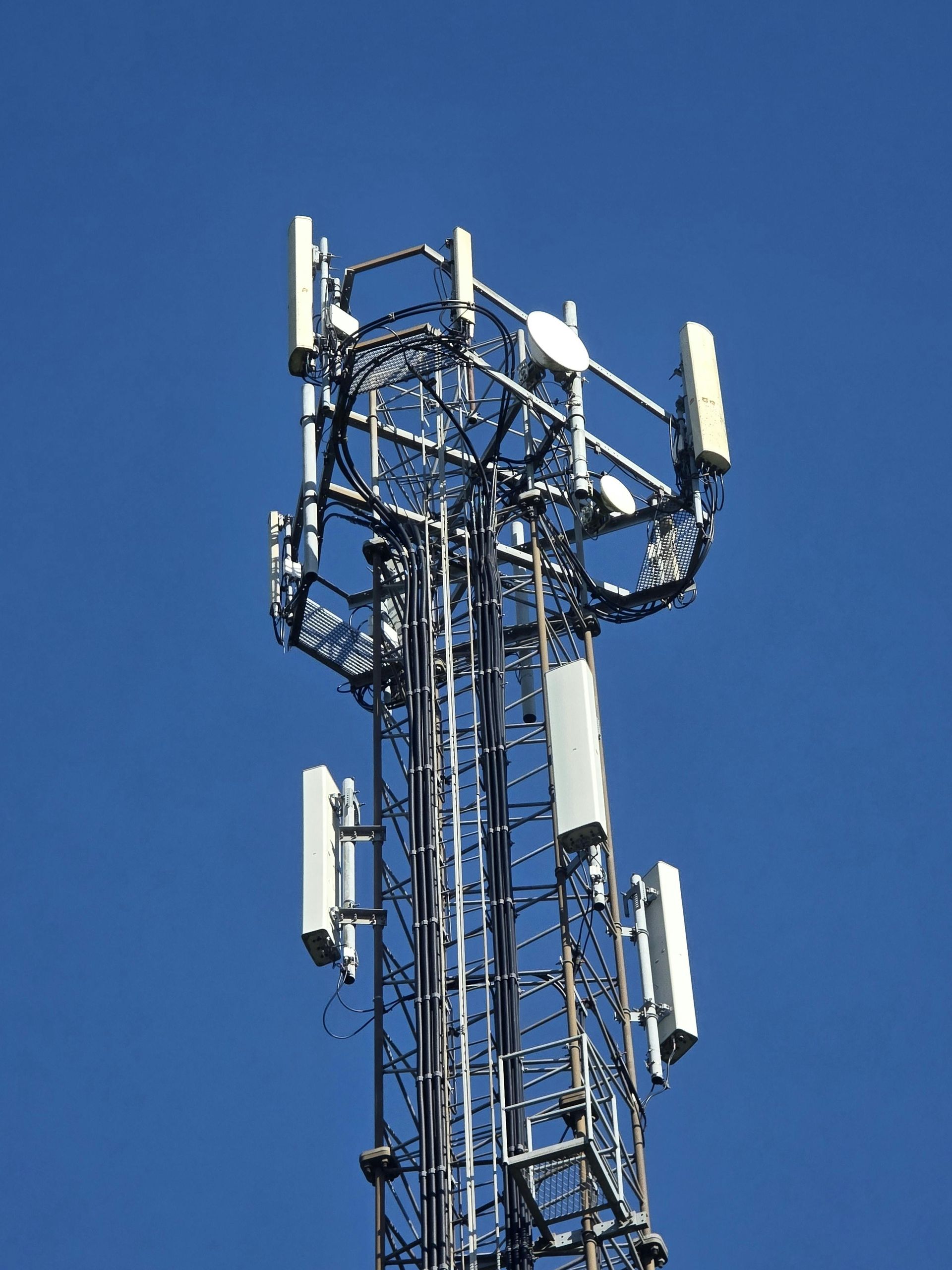 Cell tower with white antennas against a clear blue sky