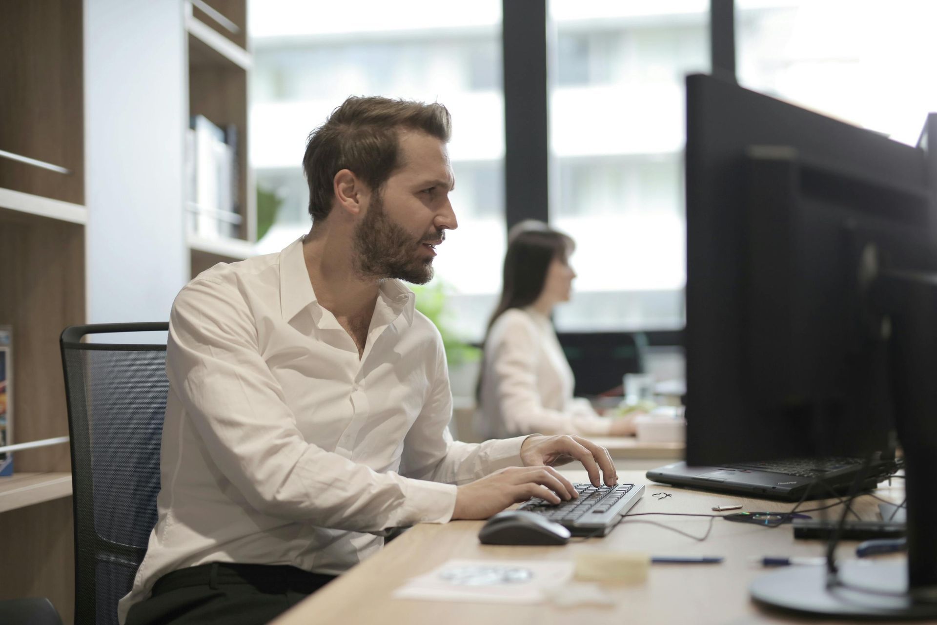 Office worker typing at a desk with dual monitors in a bright workspace