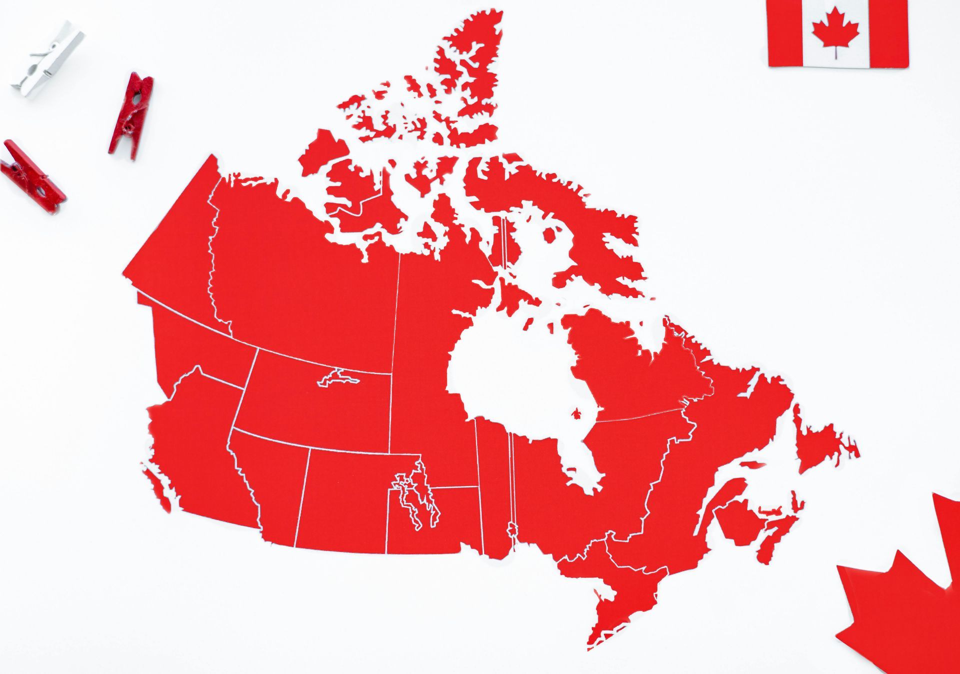 A red map of Canada on a white background, featuring red clothespins and a Canadian flag corner.