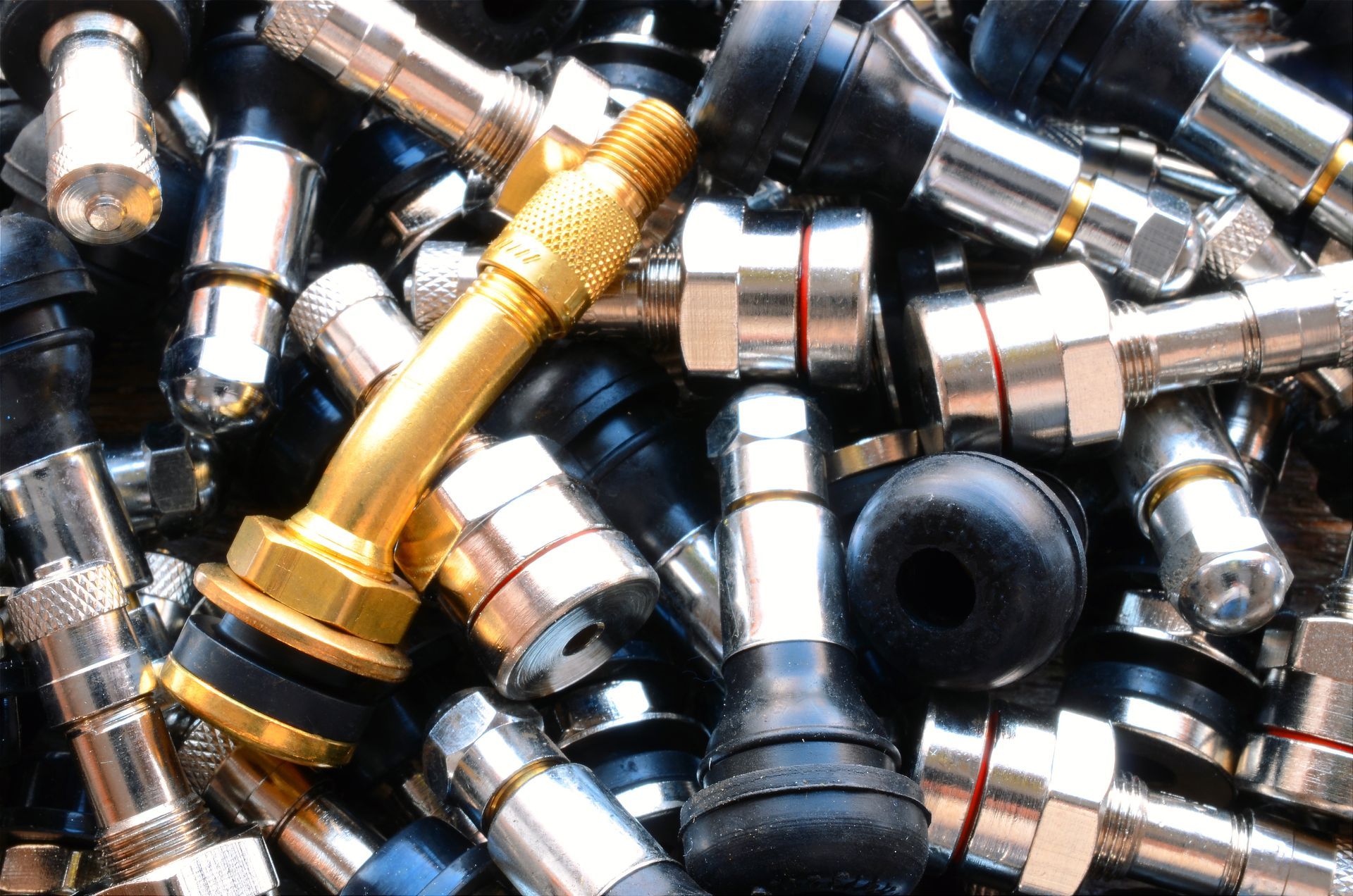Pile of tire valve stems, some silver, some black, one gold; close-up.