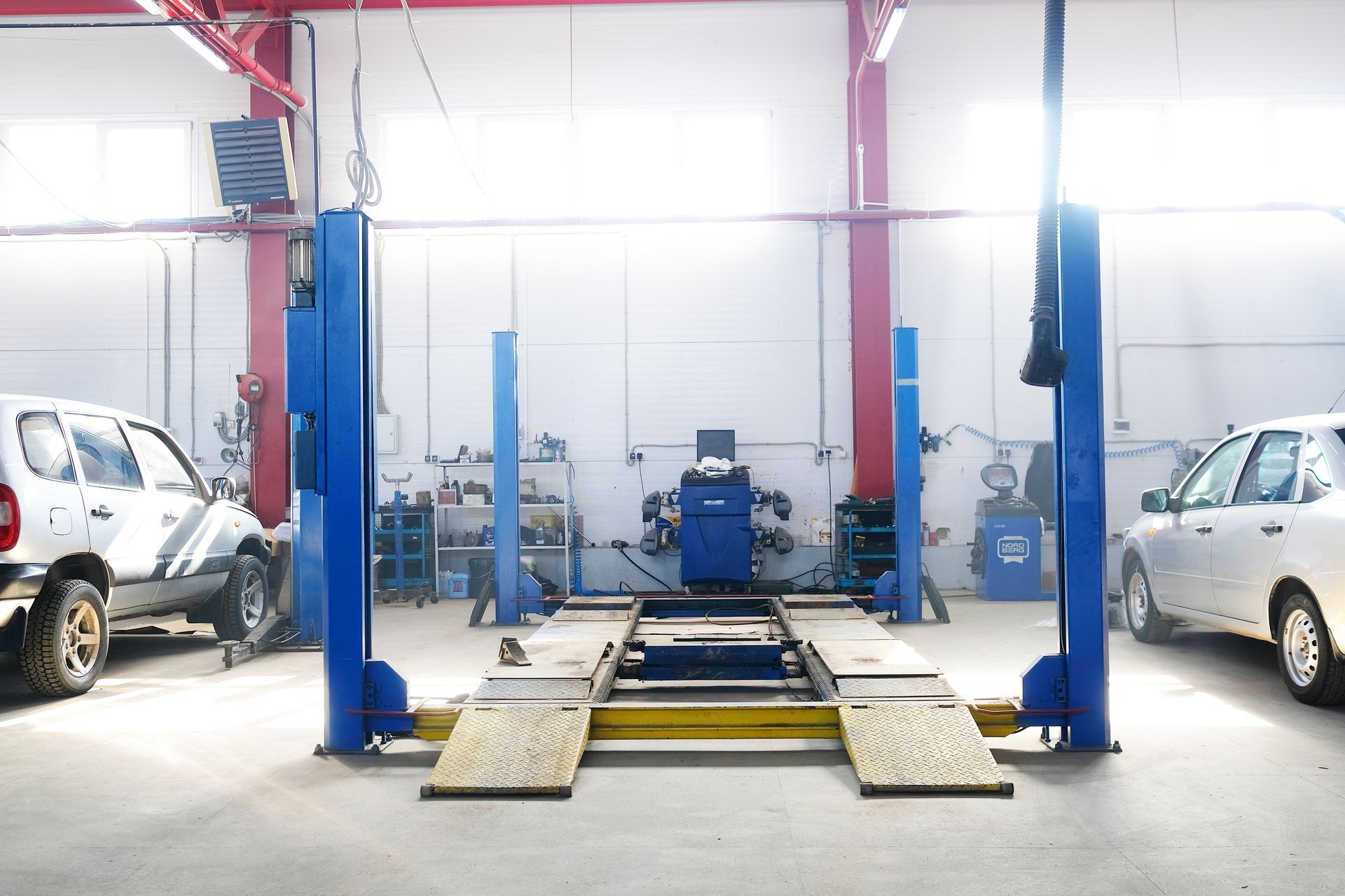 Car repair shop with blue lift, two cars, equipment, and bright lighting.