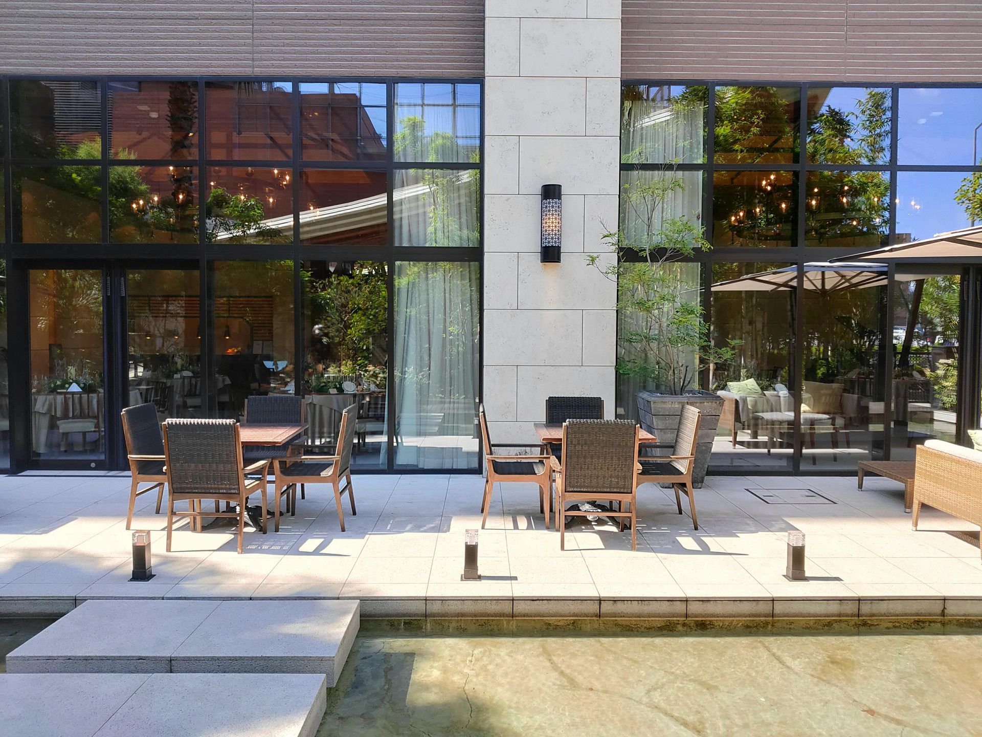 Outdoor patio with wicker chairs and tables in front of large glass windows and doors