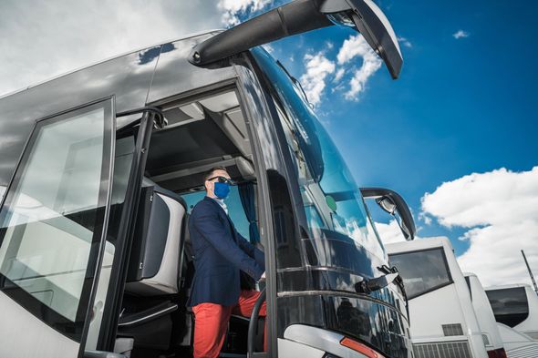 Person boarding a glossy tour bus under a blue sky