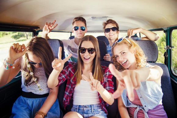 Group of friends smiling and making peace signs inside a van, with sunglasses and casual clothes