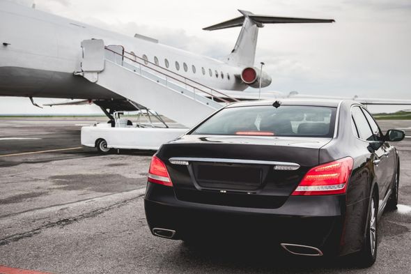 Black sedan parked beside a private jet on a wet tarmac