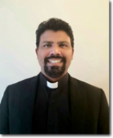 A man with a beard is wearing a black suit and a white collar.