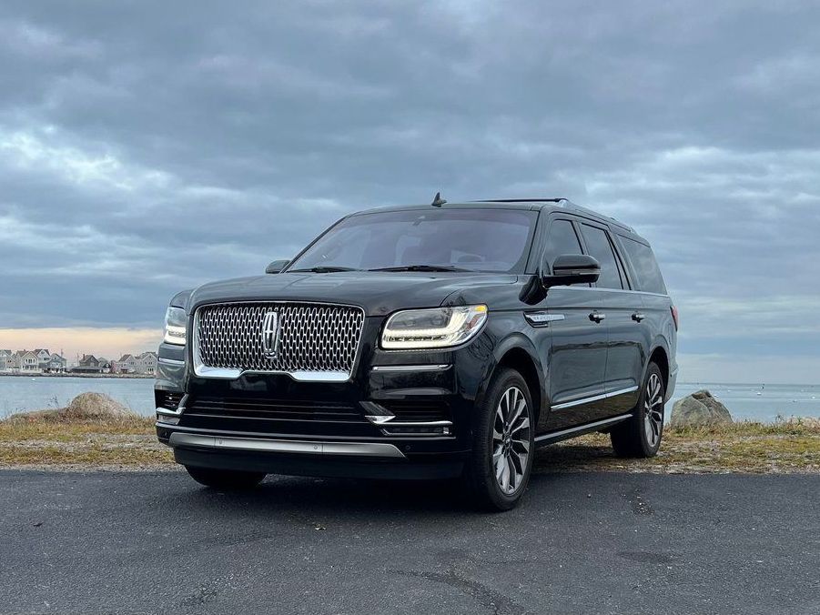 A black lincoln navigator is parked on the side of the road near the ocean.