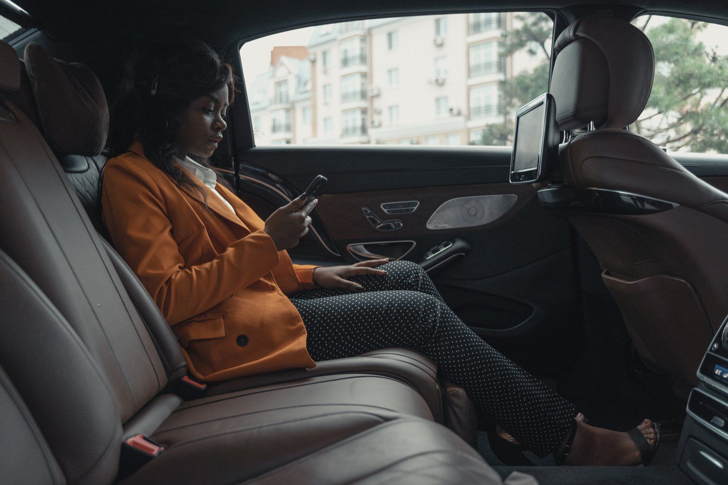 A woman is sitting in the back seat of a car looking at her phone.