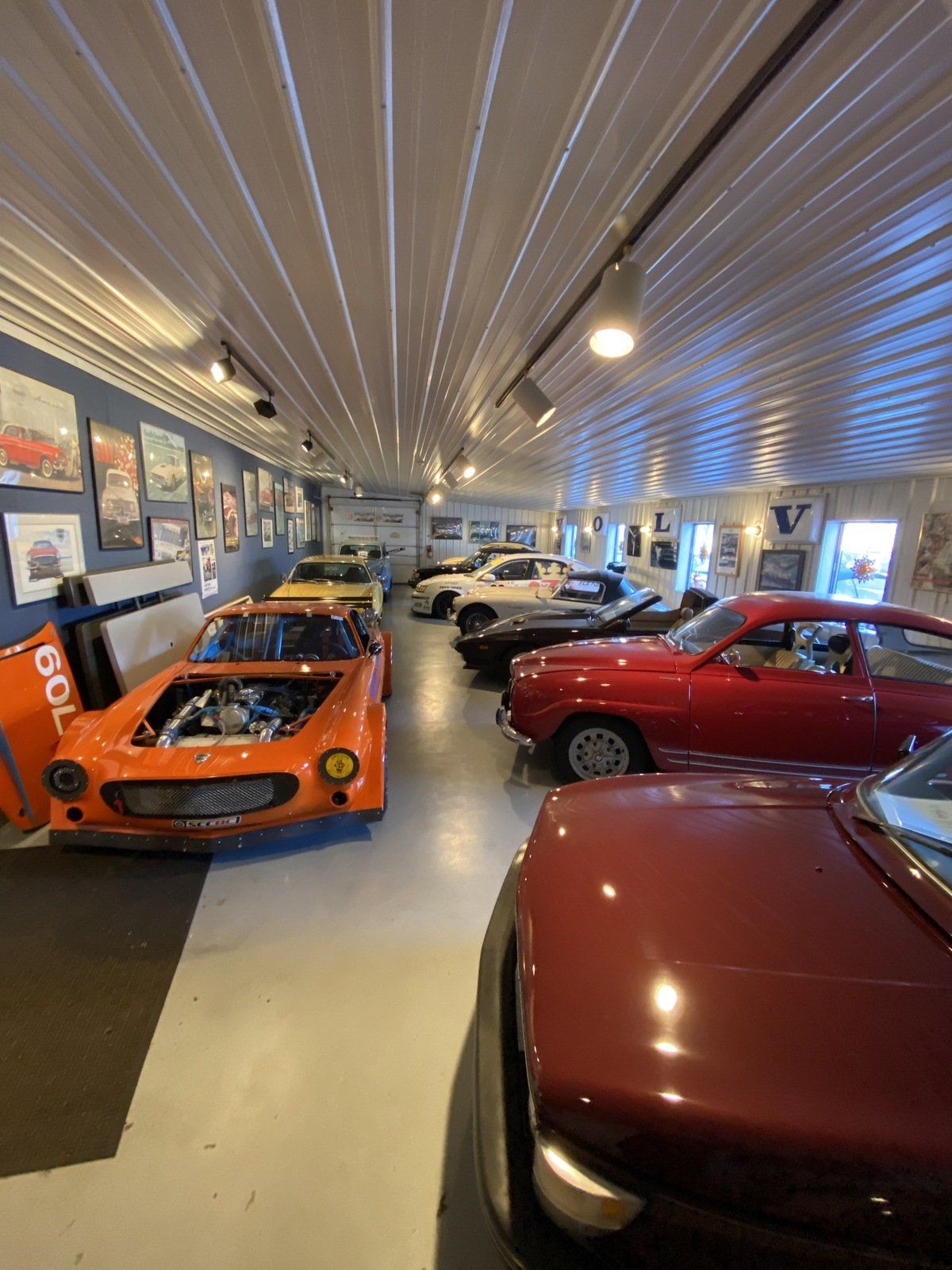 Classic cars displayed in a museum garage, including an orange race car and red vintage car.