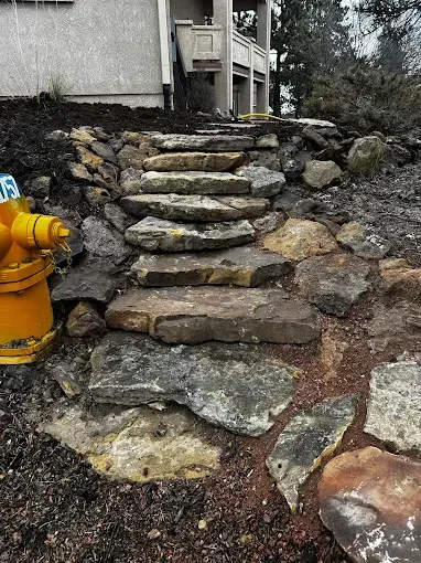 Stone steps leading up a hillside, beside a yellow fire hydrant and a building.
