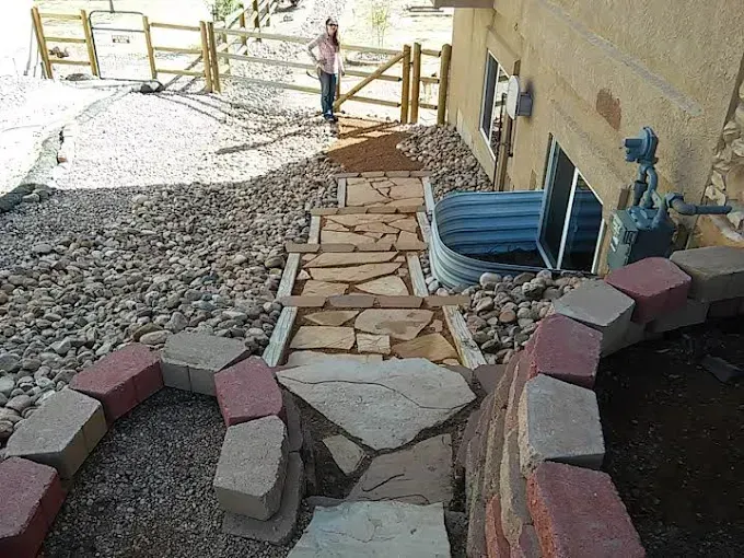 Stone steps lead up a hillside next to a house; a person stands near a wooden fence.