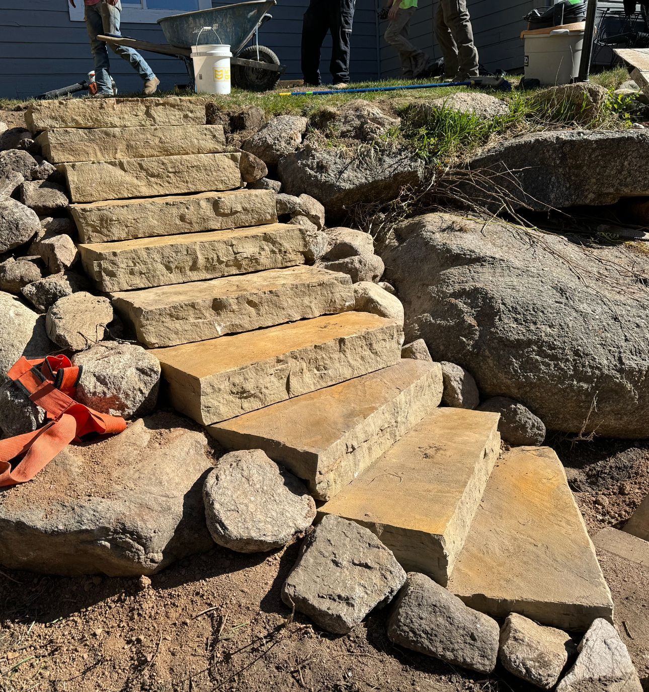 Stone steps under construction between large rocks, with workers visible at the top.