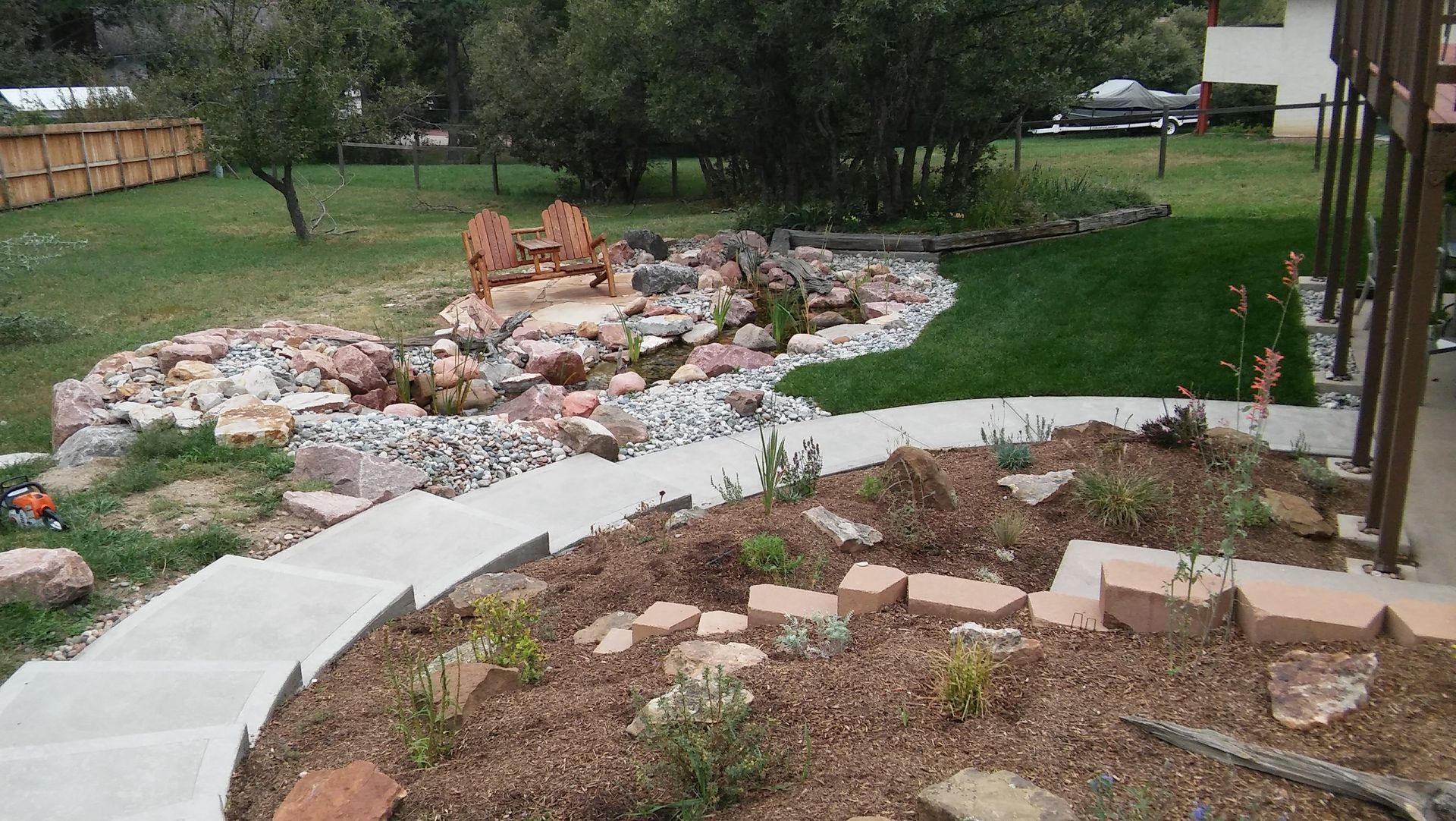 Curved garden bed with rocks, brick edging, and a small pond beside a grassy yard