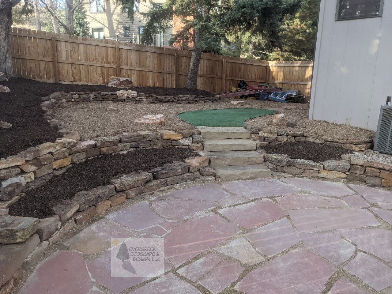 Backyard patio with stone steps, retaining walls, and a wooden fence beside a house